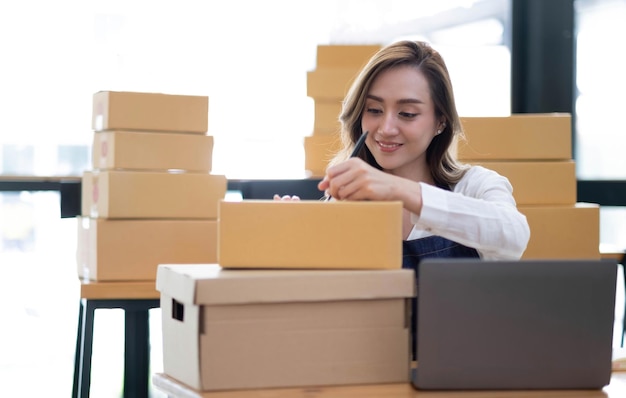 Retrato de una joven PYME asiática que trabaja con una caja en casa, el lugar de trabajo, propietario de una pequeña empresa, emprendedor de pequeñas empresas, PYME o negocio independiente en línea y concepto de entrega