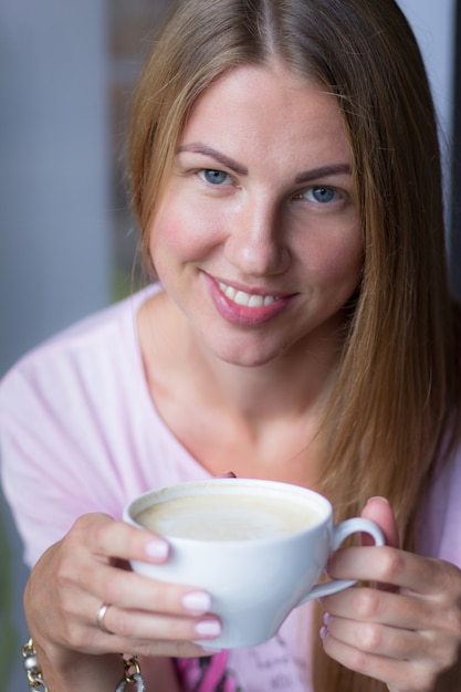 Foto retrato de una joven que bebe capuchino de una gran taza blanca