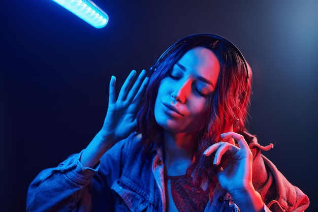 Retrato de una joven que escucha música con auriculares en neón rojo y azul en el estudio
