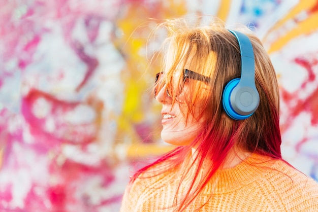 Retrato de una joven que se ríe con aparatos ortopédicos escuchando música con auriculares en el verano en la calle