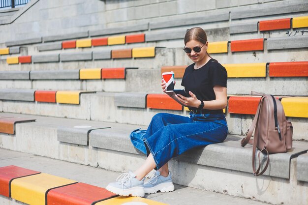 Retrato de una joven relajada sentada afuera en la ciudad con su teléfono inteligente mirando hacia otro lado y sonriendo