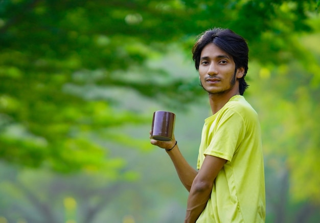 Retrato de un joven relajado sosteniendo una taza de café y respirando al aire libre en un parque