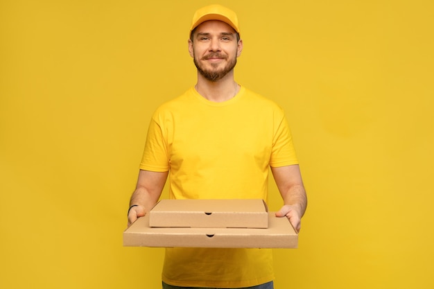 Retrato de joven repartidor en uniforme amarillo con cajas de pizza aisladas sobre pared amarilla