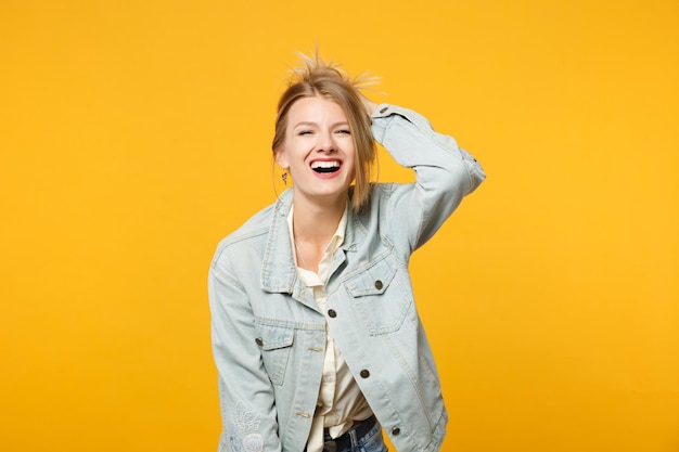 Retrato de una joven riendo con ropa informal de denim mirando hacia arriba y poniendo la mano en la cabeza aislada en un fondo de pared naranja amarillo brillante en el estudio. Concepto de estilo de vida de las personas. Simulacros de espacio de copia.
