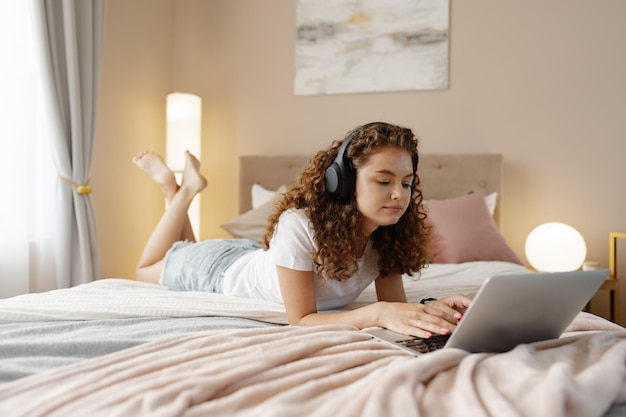 Retrato de una joven rizada usando una laptop en la cama en casa