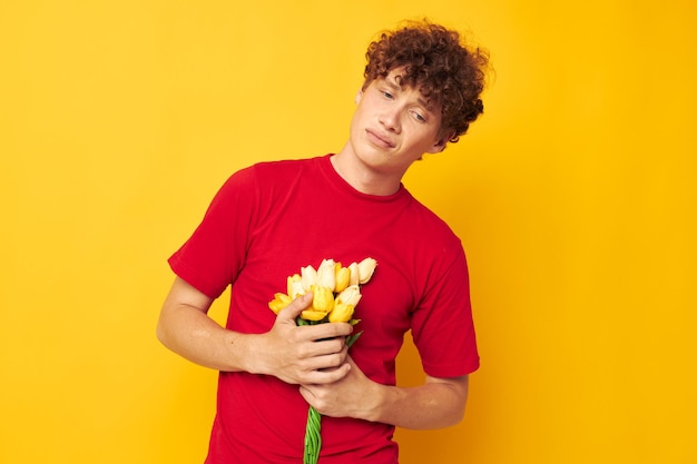 Retrato de un joven rizado con una camiseta roja, un ramo de flores, regalo de vacaciones, tiro monocromático