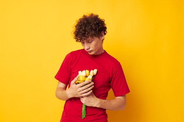 Retrato de un joven rizado con una camiseta roja, un ramo de flores, regalo de vacaciones, tiro monocromático