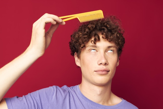 Retrato de un joven rizado posando cepillo para el cabello cuidado personal fondo rojo.