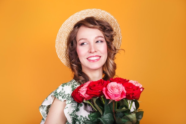 Retrato de joven romántica en vestido y sombrero de paja con ramo de rosas sobre fondo amarillo