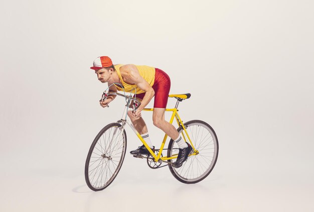 Retrato de un joven con ropa colorida y uniforme montando en bicicleta aislado sobre un corredor de fondo gris