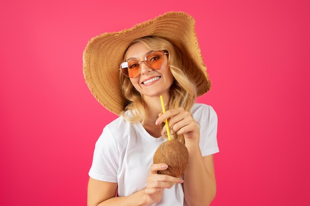 Retrato de una joven rubia alegre sosteniendo un cóctel de coco