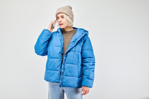 Retrato de una joven rubia con chaqueta azul hablando por teléfono móvil con cara sonriente feliz Persona con teléfono inteligente aislada sobre fondo blanco