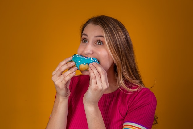 Foto retrato de una joven rubia comiendo unas deliciosas donas de colores.