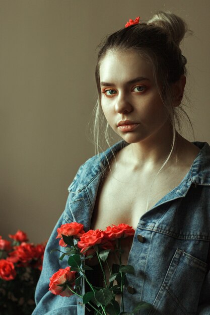 Retrato de una joven rubia con maquillaje rojo en una chaqueta vaquera y un ramo de rosas