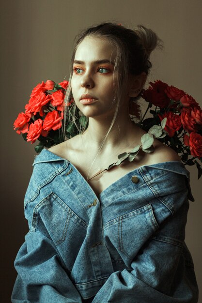 Foto retrato de una joven rubia con maquillaje rojo en una chaqueta vaquera y un ramo de rosas