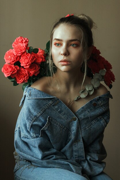 Retrato de una joven rubia con maquillaje rojo en una chaqueta vaquera y un ramo de rosas