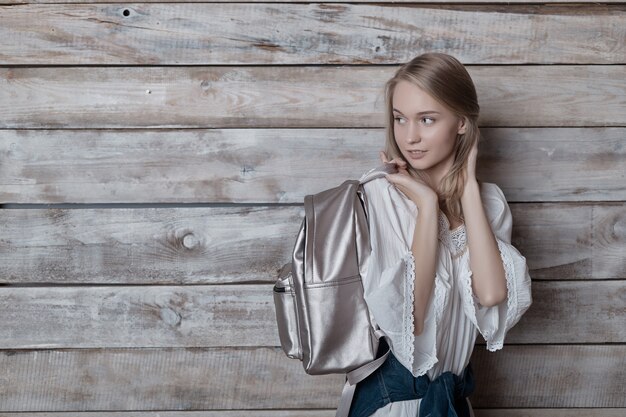 Retrato joven rubia con mochila de plata mirando a la pared de madera