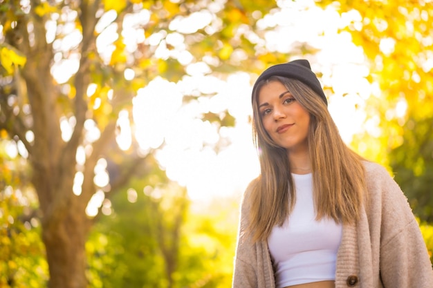 Retrato de una joven rubia con un sombrero de lana en otoño caminando por el parque al atardecer