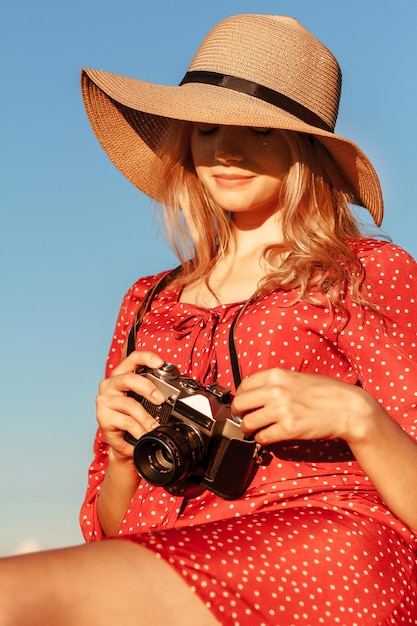 Retrato de una joven rubia con un sombrero de paja y un vestido rojo sosteniendo una cámara