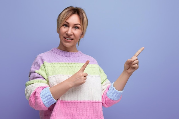 Retrato de una joven rubia sonriente y agradable con un atuendo informal que muestra una pared con un dedo en