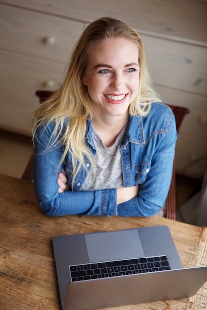 Retrato de una joven rubia sonriente con una computadora portátil y mirando hacia arriba