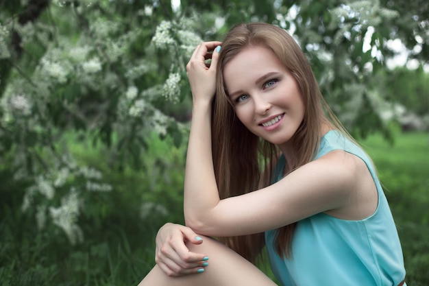 Retrato de una joven rubia con un vestido azul. árboles en flores.