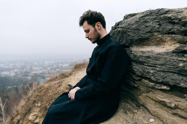 Retrato de un joven sacerdote o pastor católico cristiano serio con una túnica negra al aire libre