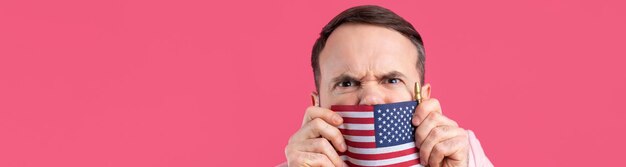 Retrato de un joven satisfecho con barba con una bandera estadounidense sobre un fondo de estudio rojo Gran patriota estadounidense y defensor de la libertad