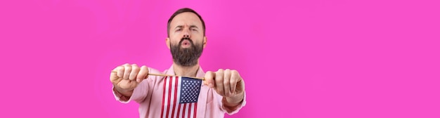 Retrato de un joven satisfecho con barba con una bandera estadounidense sobre un fondo de estudio rojo Gran patriota estadounidense y defensor de la libertad