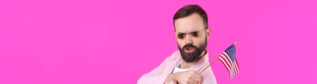 Retrato de un joven satisfecho con barba con una bandera estadounidense sobre un fondo de estudio rojo Gran patriota estadounidense y defensor de la libertad