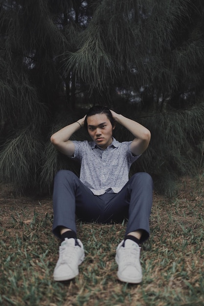 Foto retrato de un joven sentado contra los árboles en el bosque