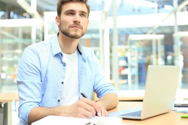 Foto retrato de joven sentado en su escritorio en la oficina.