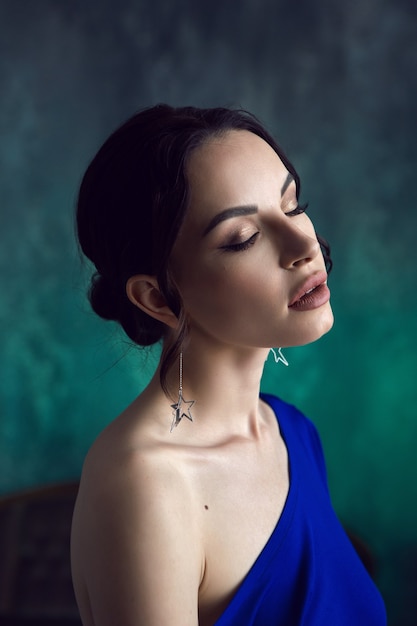 Retrato de una joven sexy con aretes en forma de estrellas con un vestido azul contra la pared gastada