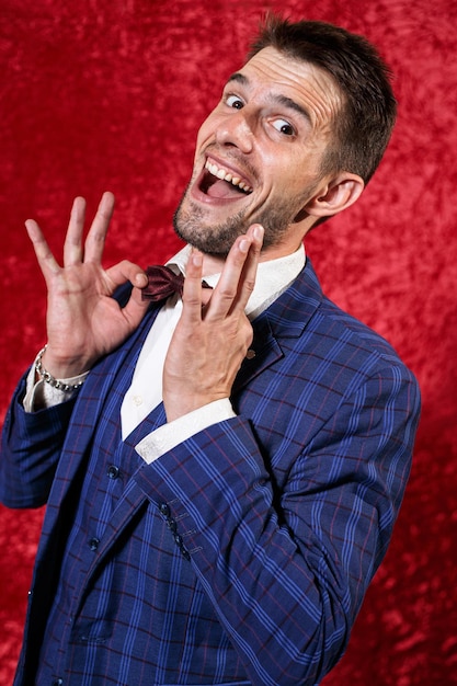 Retrato de un joven showman sonriente con traje ajustando la pajarita y mirando a la cámara