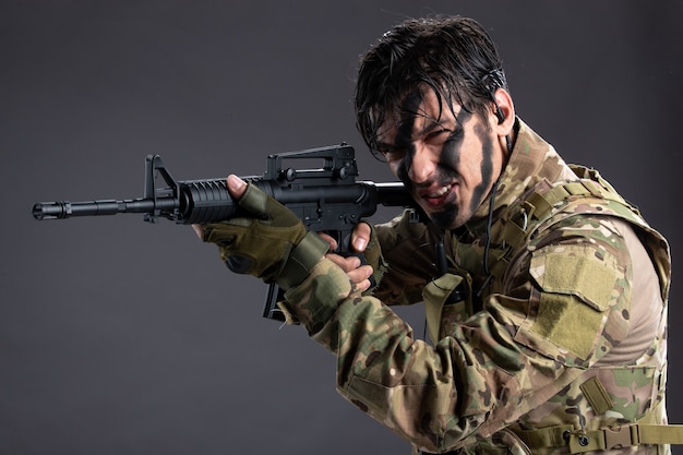 Retrato de joven soldado en camuflaje con el objetivo de ametralladora en la pared oscura