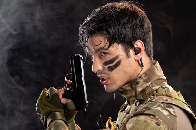 Retrato de joven soldado de camuflaje con pistola en la pared negra
