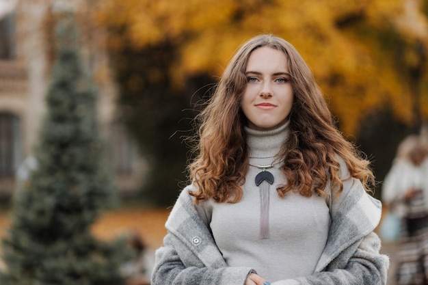 Retrato de joven sonriente con un abrigo gris en el parque de otoño