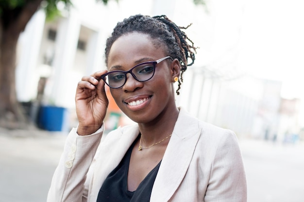 Retrato de una joven sonriente agarrando sus gafas al aire libre