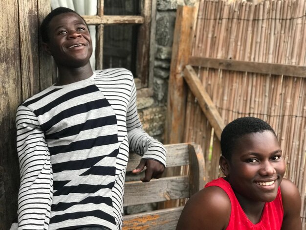 Foto retrato de un joven sonriente con un amigo contra una casa de madera