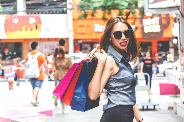 Foto retrato de una joven sonriente con bolsas de compras de pie en la acera