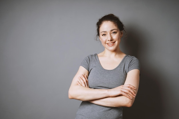 Retrato de una joven sonriente con los brazos cruzados contra un fondo gris