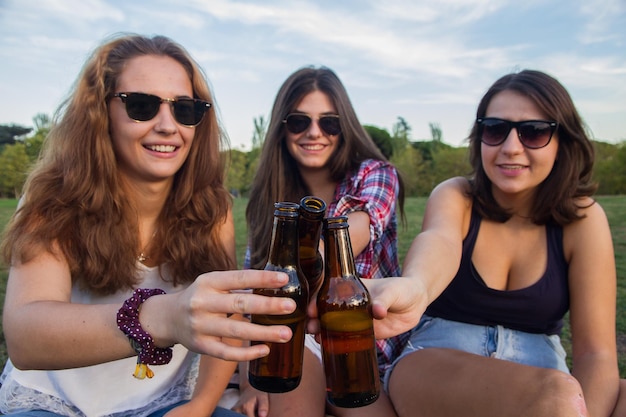 Foto retrato de una joven sonriente brindando botellas de alcohol mientras está sentada en el campo