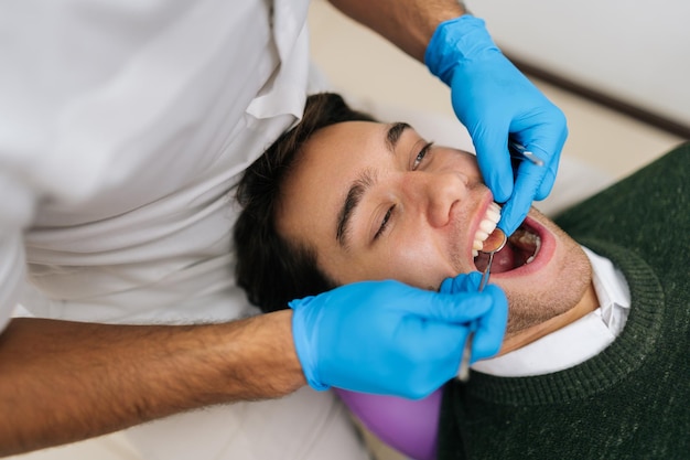 Retrato de un joven sonriente con los dientes revisados por un dentista durante una cita en una clínica dental