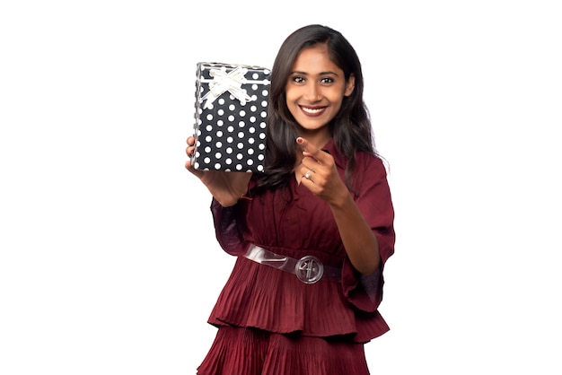 Retrato de joven sonriente feliz chica en vestido rojo sosteniendo y posando con caja de regalo sobre fondo blanco.