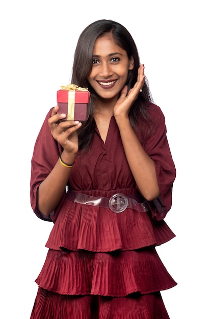 Retrato de joven sonriente feliz chica en vestido rojo sosteniendo y posando con caja de regalo sobre fondo blanco.