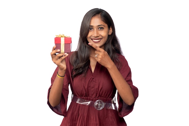 Retrato de joven sonriente feliz chica en vestido rojo sosteniendo y posando con caja de regalo sobre fondo blanco.