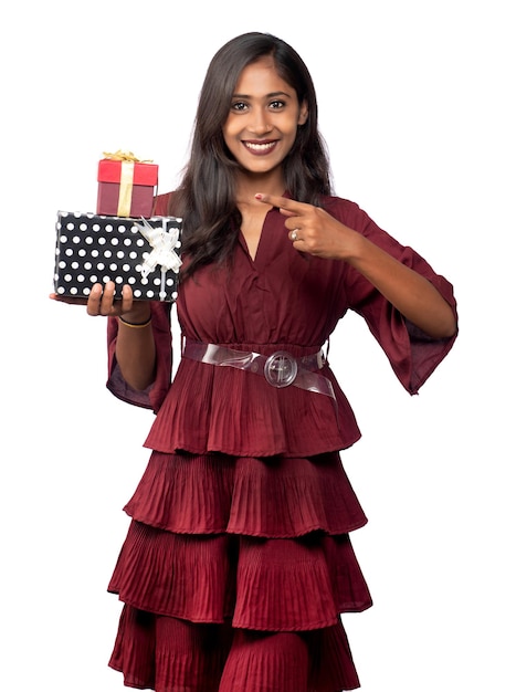 Retrato de joven sonriente feliz chica en vestido rojo sosteniendo y posando con caja de regalo sobre fondo blanco.