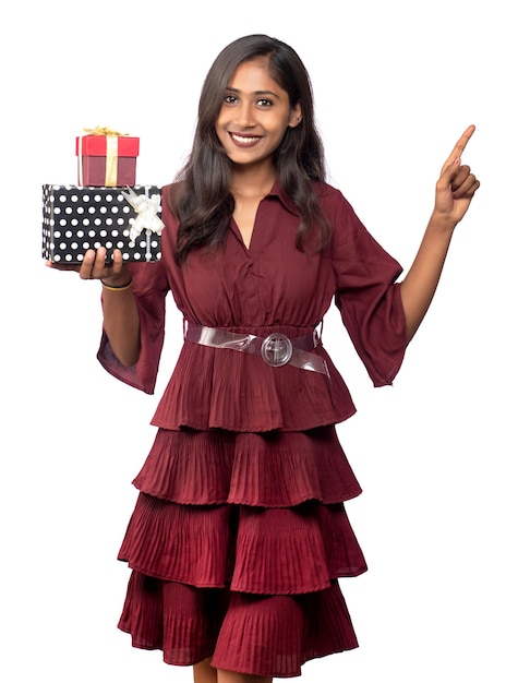 Retrato de joven sonriente feliz chica en vestido rojo sosteniendo y posando con caja de regalo sobre fondo blanco.