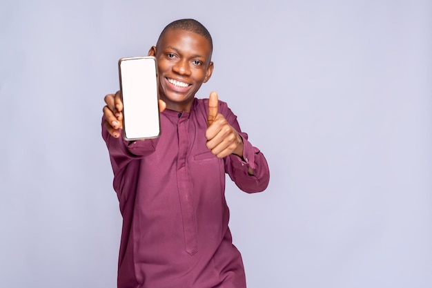 Retrato joven sonriente feliz negro hombre africano de 20 años en espera en la mano usar teléfono celular móvil con área de trabajo de pantalla en blanco mostrar gesto de golpe aislado en estudio de fondo blanco liso