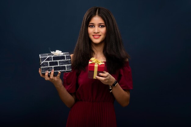 Retrato de una joven sonriente feliz sosteniendo y posando con una caja de regalo en un fondo gris